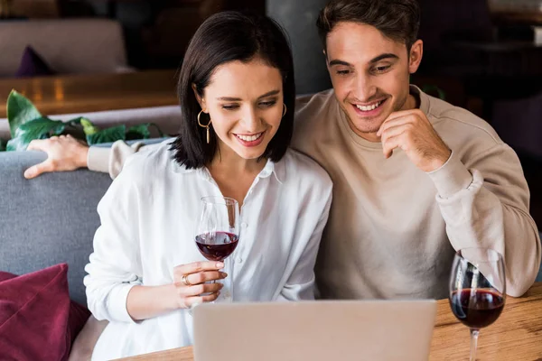 Feliz hombre y mujer con copa de vino mirando a la computadora portátil - foto de stock