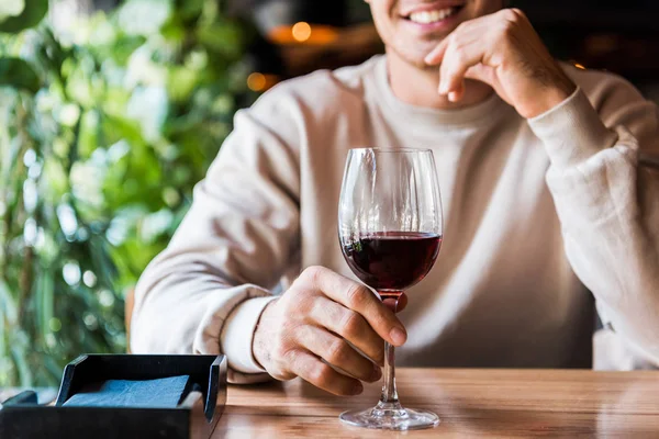 Vue recadrée de l'homme joyeux assis au restaurant avec un verre de vin — Photo de stock