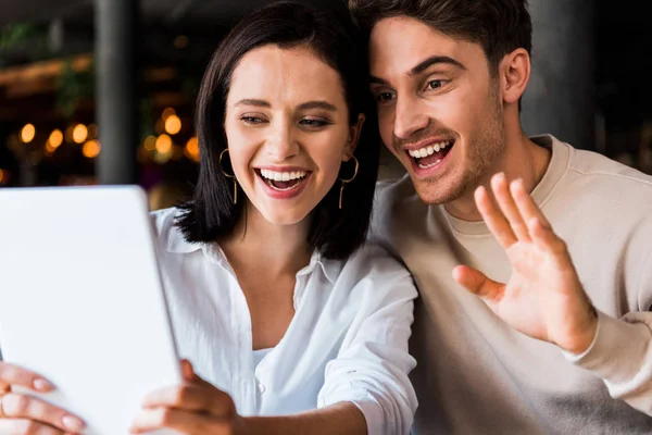 Mulher feliz olhando para tablet digital perto de homem alegre acenando mão — Fotografia de Stock