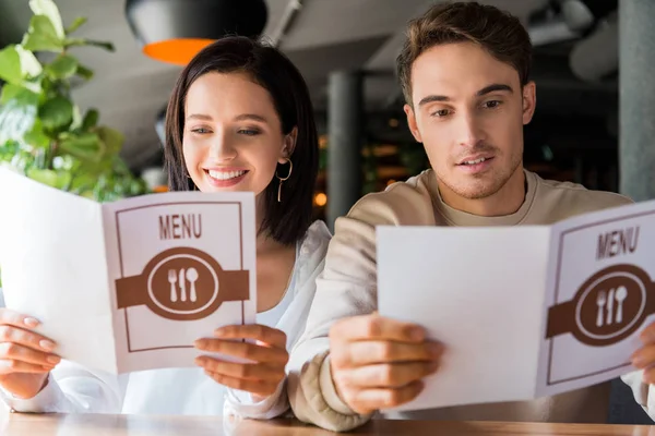 Selective focus of happy man and smiling woman looking at menus in restaurant — Stock Photo