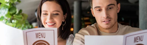 Panoramic shot of man and happy woman looking at menus in restaurant — Stock Photo