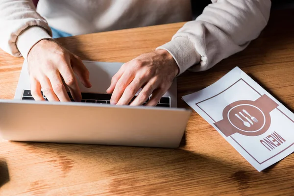 Ausgeschnittene Ansicht einer Frau, die auf dem Laptop neben dem Menü auf dem Tisch tippt — Stockfoto