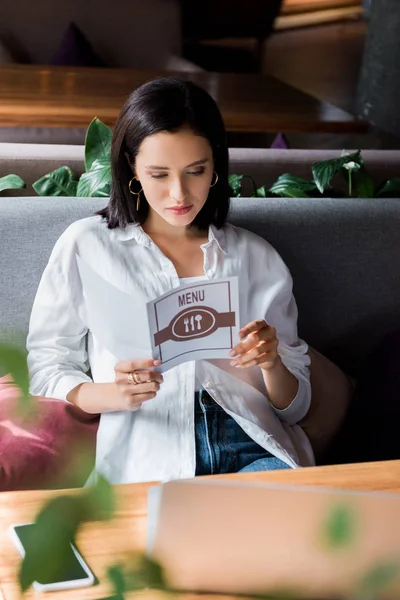 Mulher segurando menu perto de smartphone com tela em branco e laptop na mesa — Fotografia de Stock