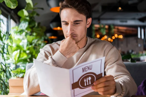 Hombre guapo tocando la cara mientras lee el menú - foto de stock