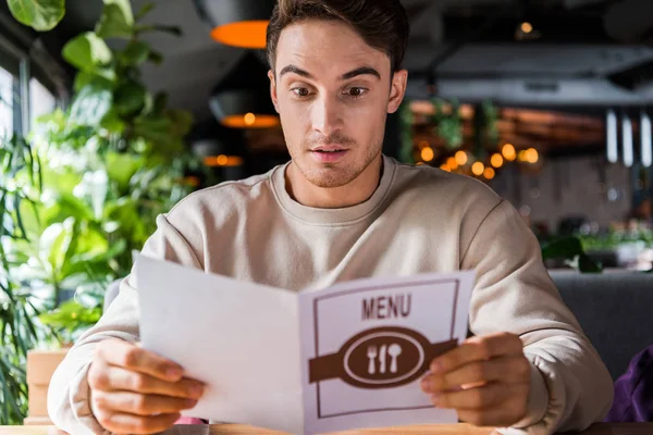 Foco seletivo de homem surpreso segurando menu no restaurante — Fotografia de Stock