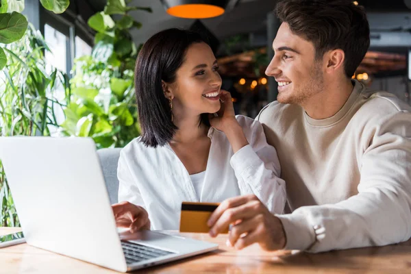 Selektiver Fokus der fröhlichen Frau, die Mann mit Kreditkarte in Laptopnähe ansieht — Stockfoto