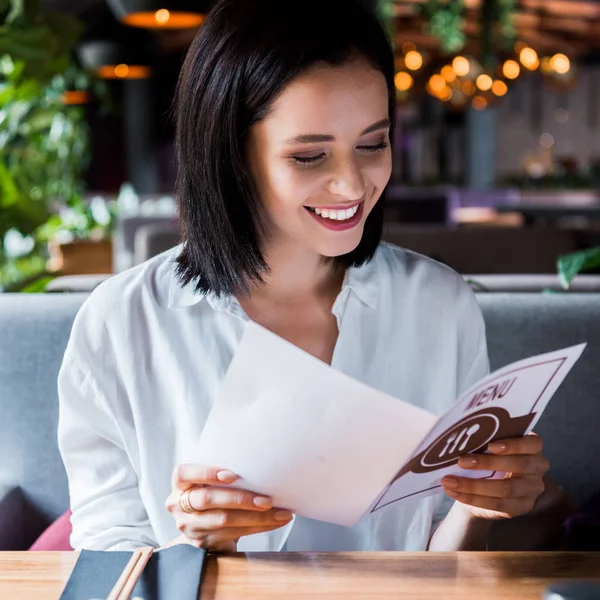 Enfoque selectivo de la mujer alegre sentado en el bar de sushi y mirando el menú - foto de stock