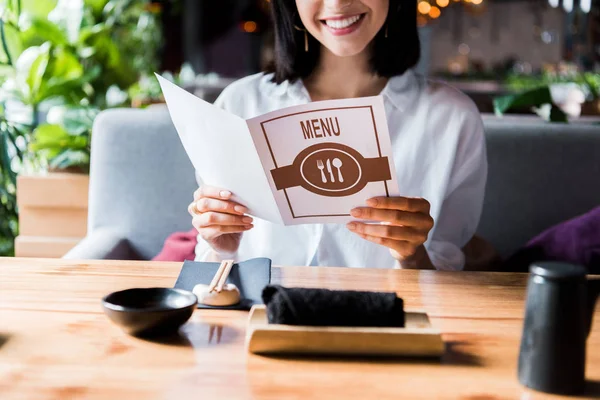 Cropped view of cheerful woman sitting in sushi bar and holding menu — Stock Photo