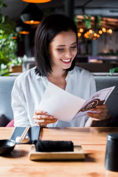 Enfoque selectivo de la mujer alegre sentado en el restaurante y mirando el menú - foto de stock