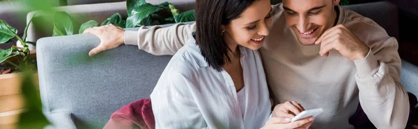 Panoramic shot of happy woman using smartphone near man in sushi bar — Stock Photo