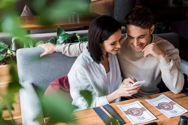 Selective focus of happy woman using smartphone near man in sushi bar — Stock Photo