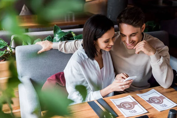 Enfoque selectivo de la mujer feliz utilizando el teléfono inteligente cerca del hombre en el bar de sushi - foto de stock