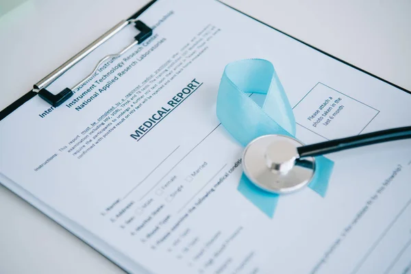 Blue awareness ribbon and stethoscope on medical report — Stock Photo