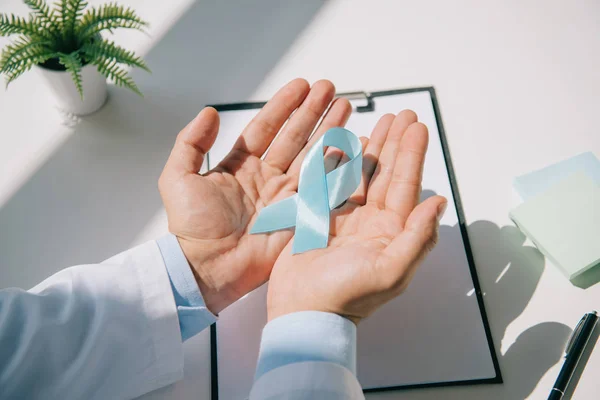 Cropped view of doctor holding blue awareness ribbon near clipboard — Stock Photo