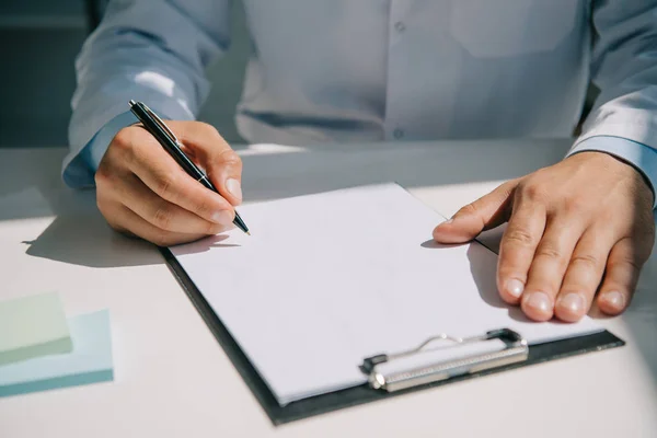 Cropped view of doctor holding pen near clipboard with blank paper — Stock Photo