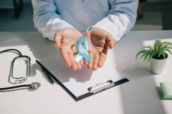 Vue recadrée du médecin montrant un ruban de sensibilisation bleu près du presse-papiers avec du papier blanc — Photo de stock