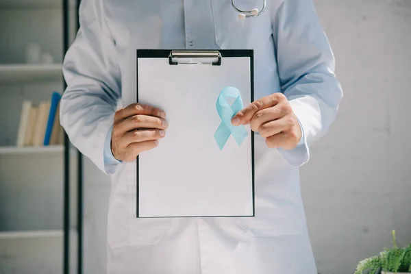 Vista recortada do médico segurando prancheta com papel em branco e fita de consciência azul — Fotografia de Stock