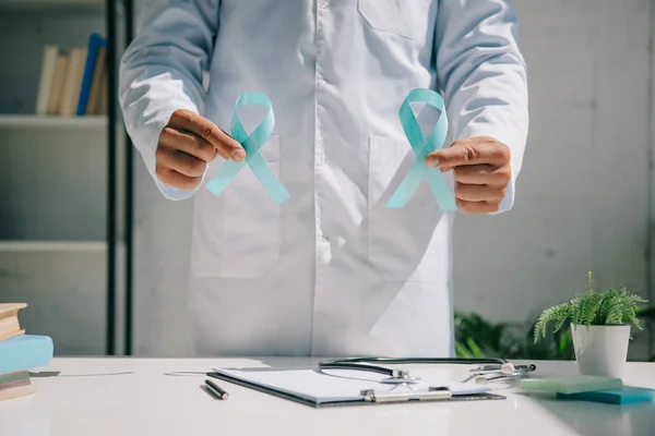 Partial view of doctor in white coat holding blue awareness ribbons — Stock Photo