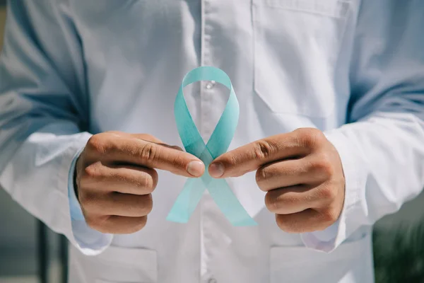 Partial view of doctor in white coat holding blue awareness ribbon — Stock Photo