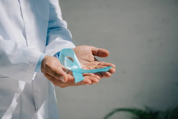 Обрізаний вид на лікаря в білому пальто, що тримає синю стрічку обізнаності — стокове фото