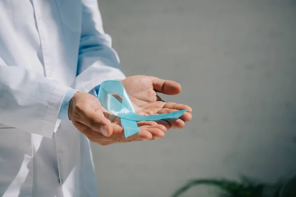 Vue recadrée du médecin en manteau blanc tenant un ruban de sensibilisation bleu — Photo de stock