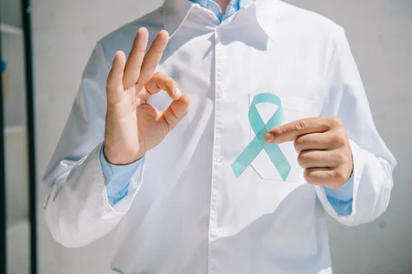 Vista recortada del médico sosteniendo la cinta azul de la conciencia y mostrando la muestra aceptable - foto de stock