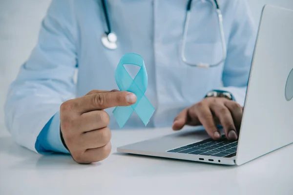 Cropped view of doctor holding blue awareness ribbon while using laptop — Stock Photo