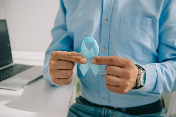 Partial view of man in blue shirt holding blue awareness ribbon — Stock Photo