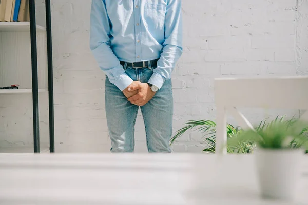 Vue recadrée de l'homme tenant les mains serrées près de la zone de l'aine tout en se tenant par un mur blanc — Photo de stock