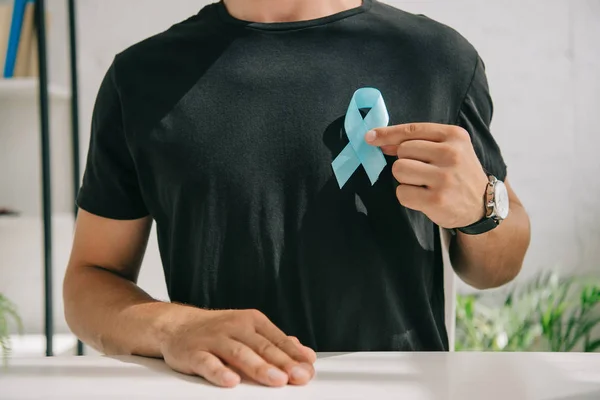 Partial view of man in black t-shirt holding blue awareness ribbon — Stock Photo