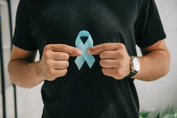 Cropped view of man in black t-shirt holding blue awareness ribbon — Stock Photo