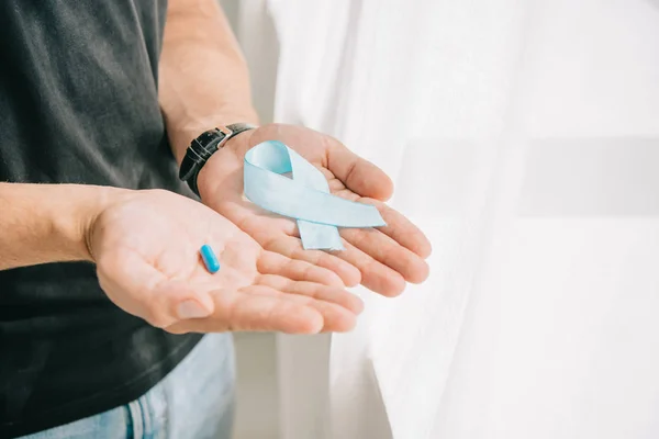 Vue partielle de l'homme tenant un ruban de conscience bleu debout près de la fenêtre — Photo de stock