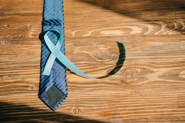 Blue awareness ribbon and tie on wooden background with copy space — Stock Photo