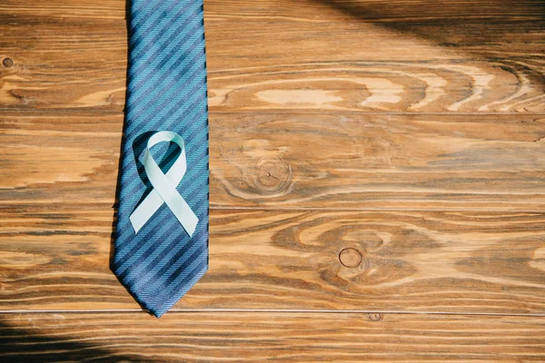 Tie and blue awareness ribbon on wooden surface — Stock Photo