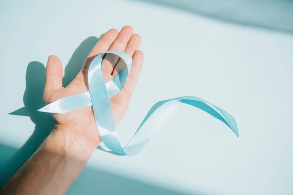 Partial view of male hand with blue awareness ribbon on white background — Stock Photo