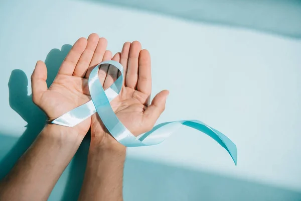 Cropped view of male hands with blue awareness ribbon on white background — Stock Photo