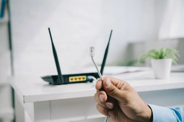 Cropped view of businessman holding wire with connector near router — Stock Photo