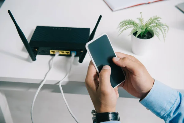 Cropped view of businessman holding smartphone near plugged router — Stock Photo