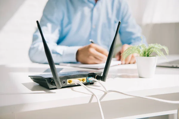 Selective focus of plugged router near businessman writing in notebook — Stock Photo