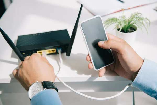 Cropped view of businessman plugging router while holding smartphone — Stock Photo