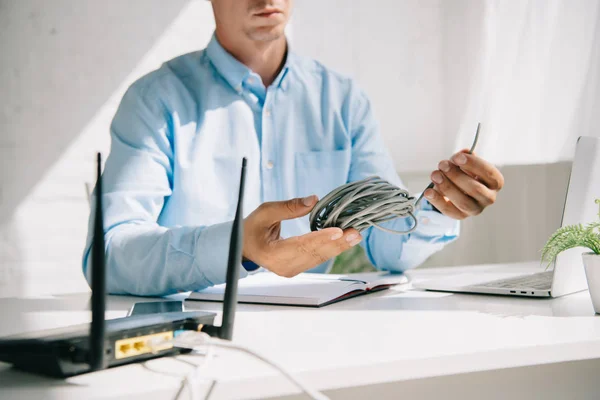 Vista recortada de hombre de negocios sosteniendo alambre cerca de router enchufado - foto de stock