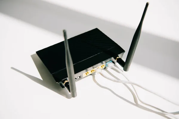 Schwarzer eingesteckter Router auf weißem Bürotisch bei Sonnenschein — Stockfoto