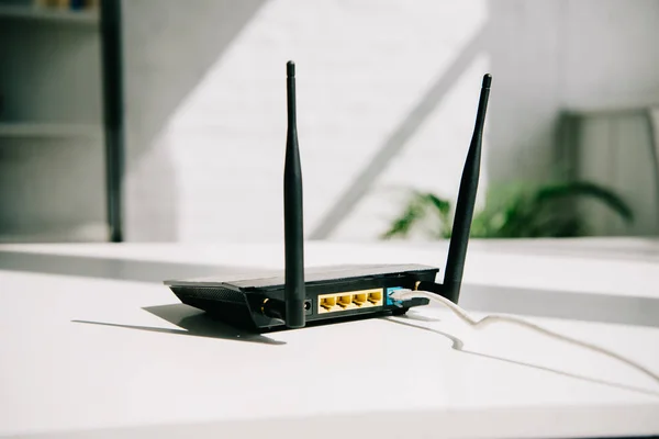 Router nero collegato su tavolo da ufficio bianco sotto il sole — Foto stock