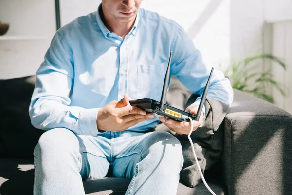 Ausgeschnittene Ansicht eines Geschäftsmannes, der auf dem Sofa sitzt und einen eingesteckten Router hält — Stockfoto