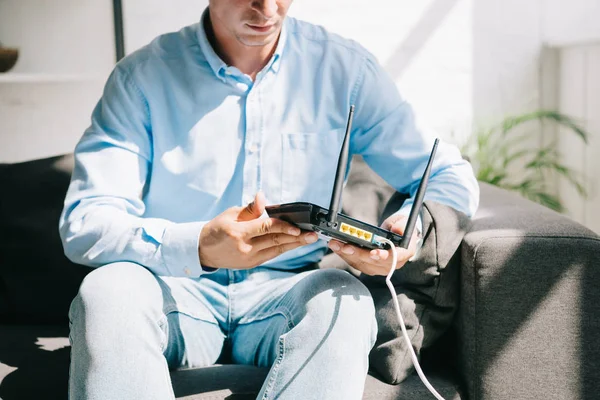 Vista recortada del hombre de negocios sentado en el sofá y la celebración de router enchufado - foto de stock