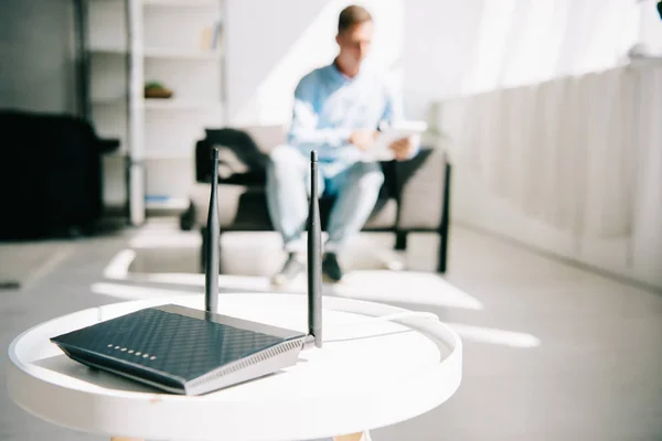 Enfoque selectivo de enrutador enchufado negro en la mesa blanca y hombre de negocios sentado en el sofá — Stock Photo