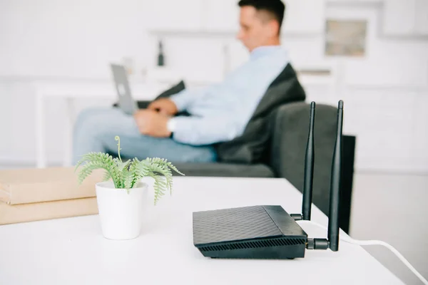 Foyer sélectif de routeur noir sur bureau blanc près de pot de fleurs et homme d'affaires à l'aide d'un ordinateur portable — Photo de stock