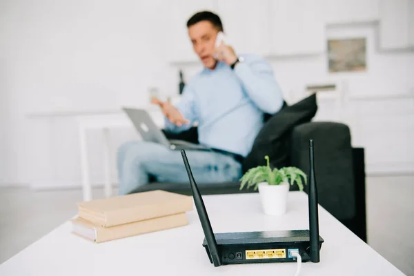 Selektiver Fokus von schwarzem Router auf weißem Tisch und Geschäftsmann im Smartphone-Gespräch — Stockfoto