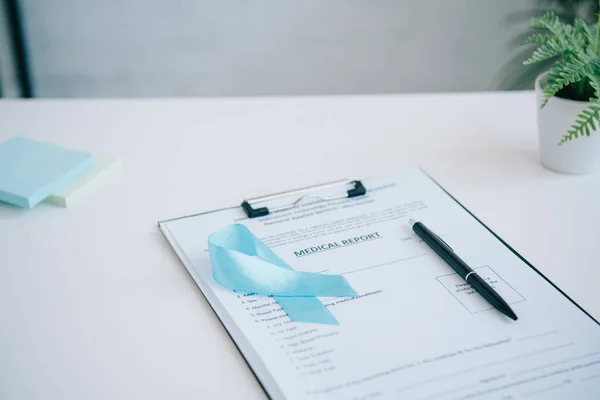 Blue awareness ribbon, medical report, pen and sticky notes on white table — Stock Photo