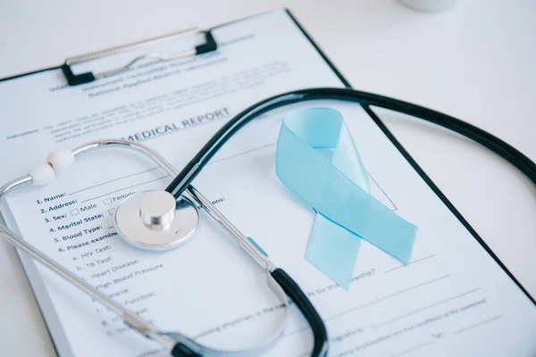 Rapport médical, stéthoscope et ruban de sensibilisation bleu sur table blanche — Photo de stock